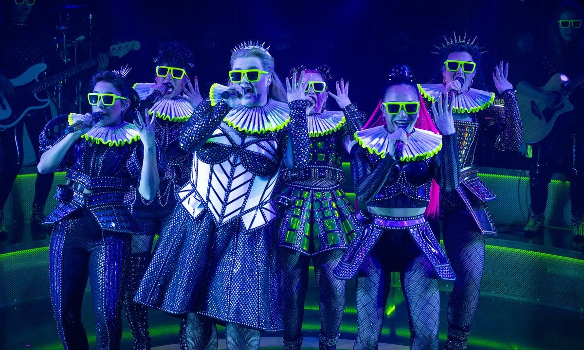 SIX the Musical cast in neon green sunglasses and ruffled collars performing under UV stage lighting